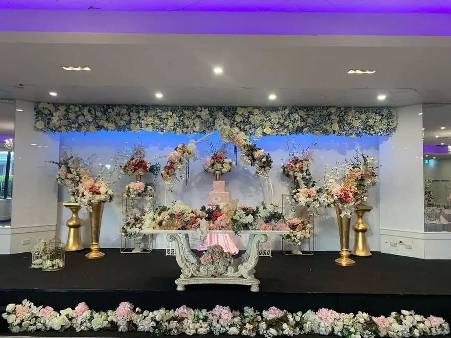 Stage with a pink tiered cake and red and pink florals