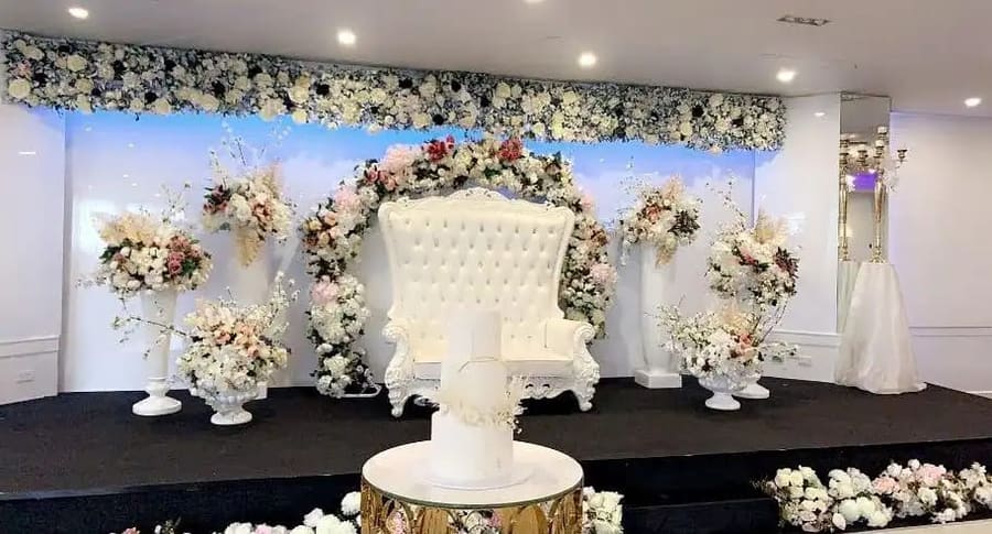 White throne chair under a floral arch, with a tiered cake
