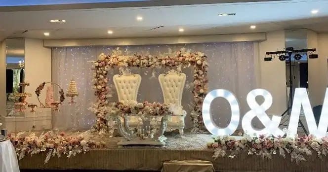 Throne chairs under a blush floral arch beside light-up O&M letters