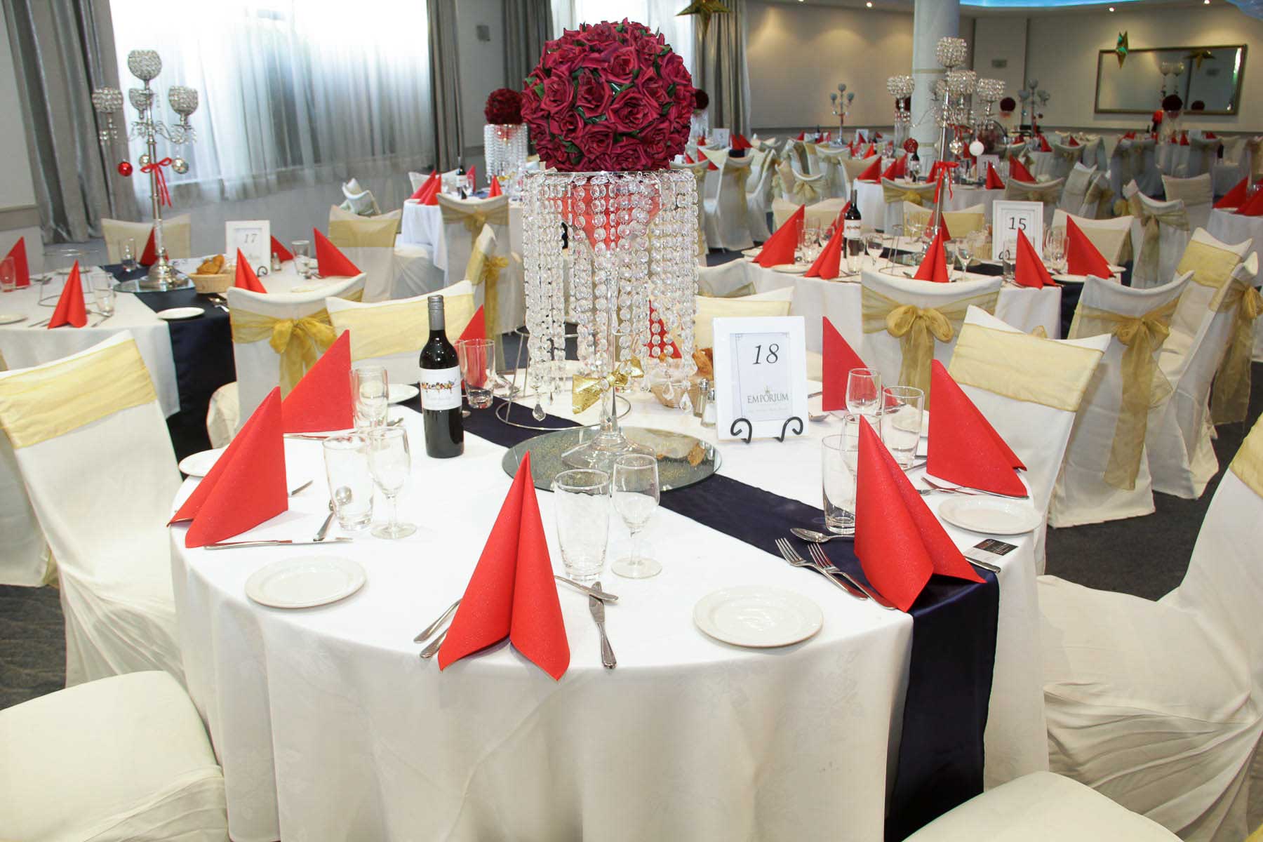Round table set with red napkins, a crystal centrepiece and an Emporium table card
