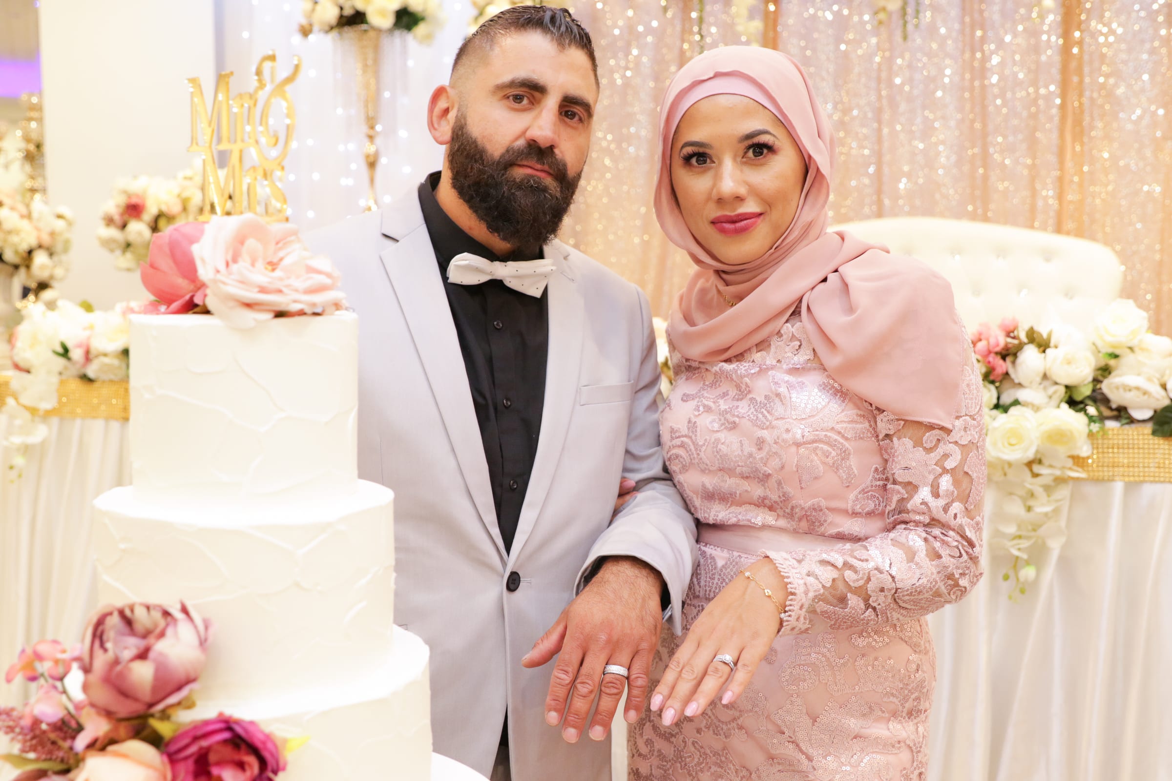 Couple beside a tiered cake and a floral wall