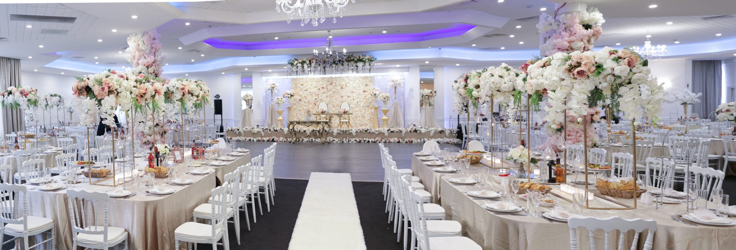 Long banquet tables either side of a white aisle, with tall gold floral stands