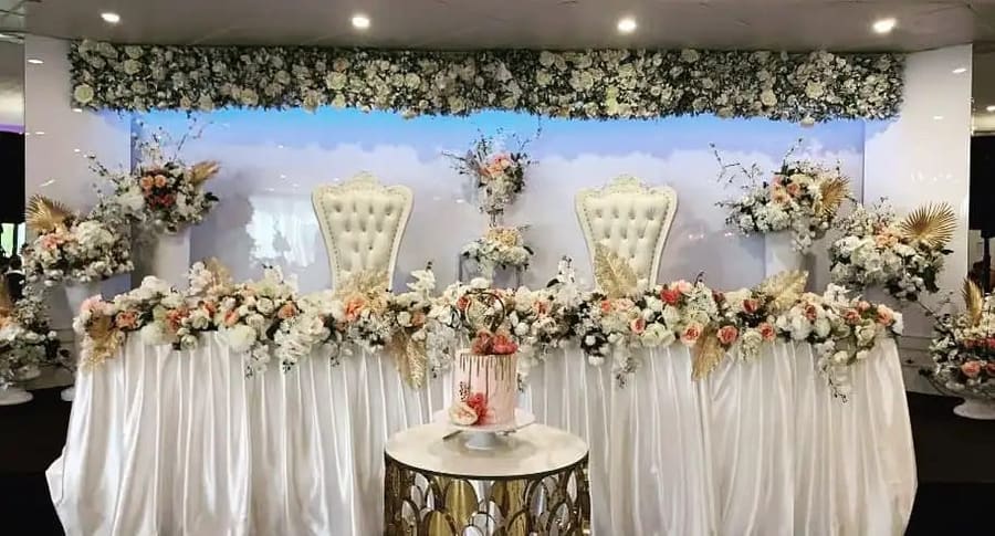 Two throne chairs at a head table under a floral wall